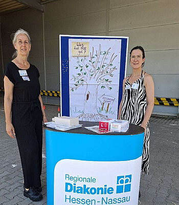 Zwei Mitarbeitende der Fachstelle Sucht vor einem Stand der Regionalen Diakonie Westerwald Rhein-Lahn.