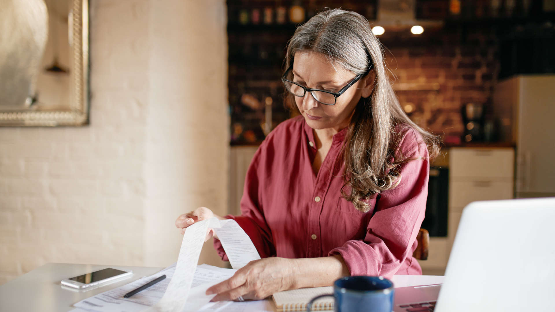 Eine Frau ordnet Papierunterlagen und betrachtet einen langen Kassenbon.