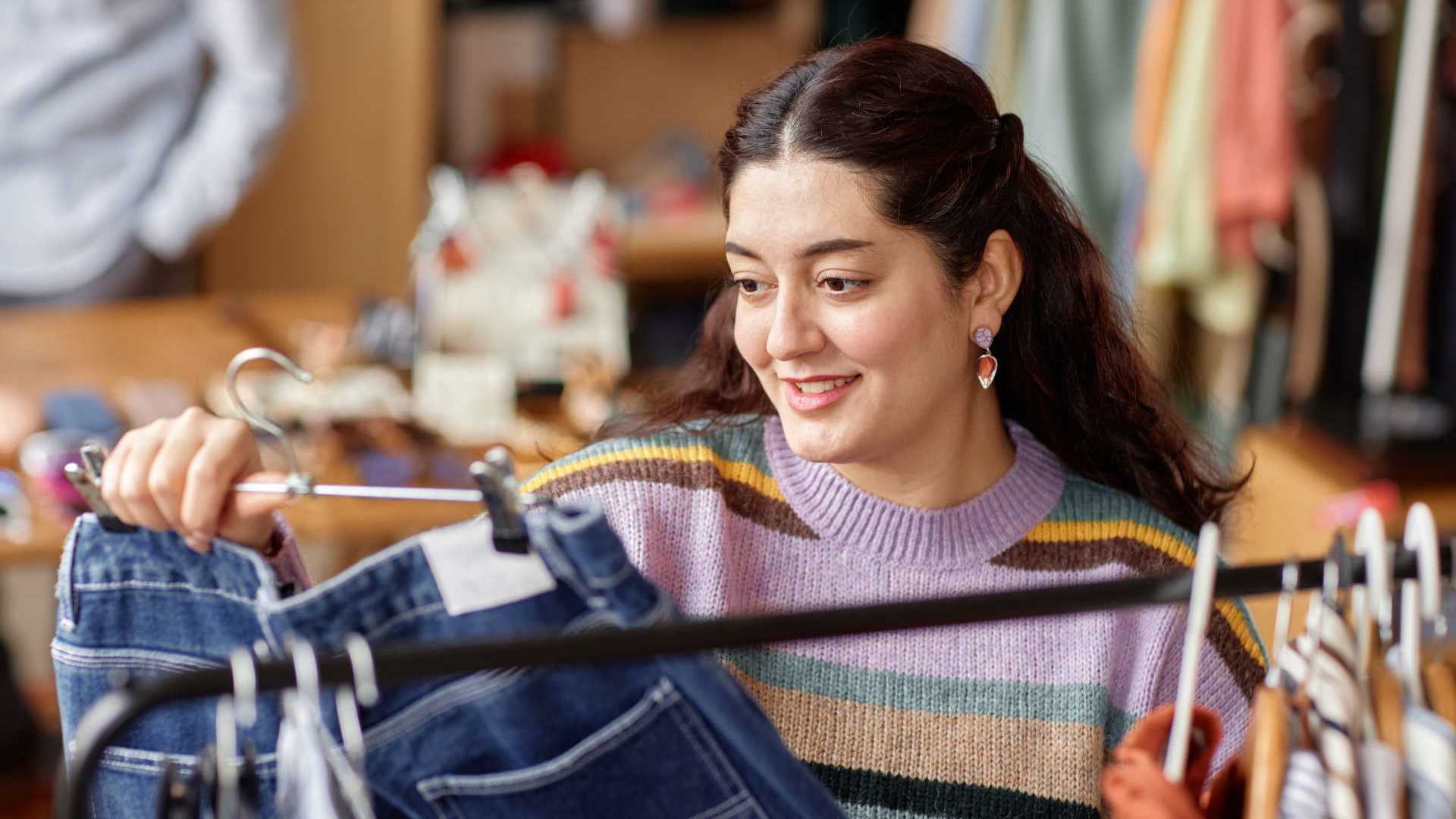 Eine Frau steht an einer Kleiderstange und betrachtet eine Jeans auf einem Bügel.