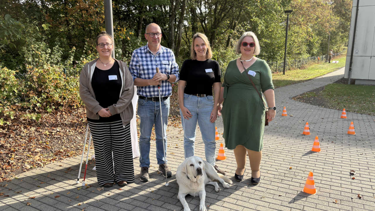 Drei Frauen, ein Mann und sein Blindenführhund schauen stehen nebeneinander.